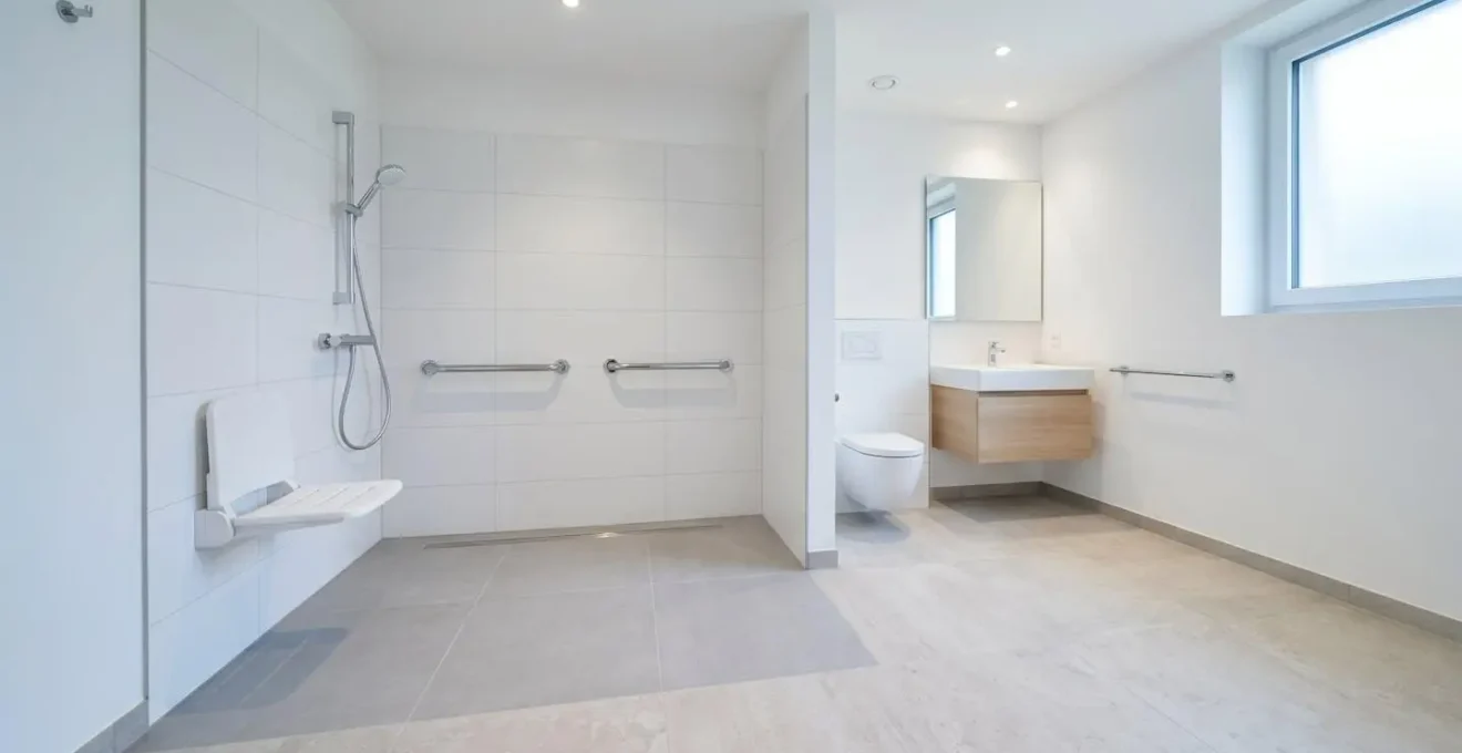 Salle de bain adaptée française avec douche à l'italienne sans ressaut, barres d'appui chromées et siège rabattable, financée par le capital premier équipement